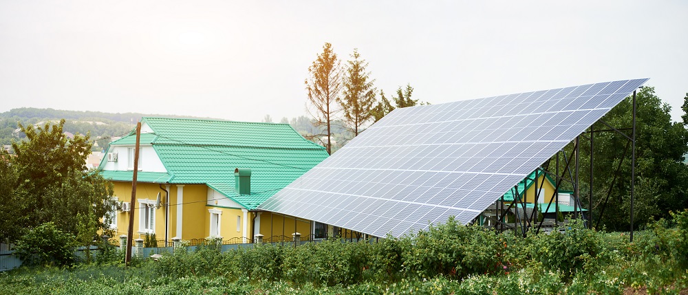 Large solar panel array, part of a Solar Panel Installation in Lafourche Parish, sits near yellow houses with green roofs amid a lush rural landscape under a cloudy sky.