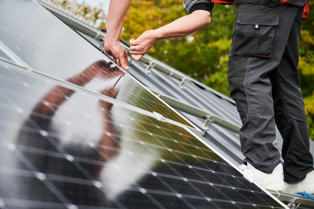 Two people, likely Solar Installers in St Charles Parish, are installing or adjusting solar panels on a rooftop with trees visible in the background.