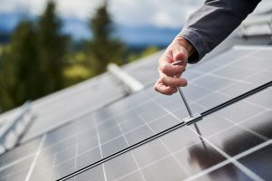 A person, like one of the expert Solar Installers in St Charles Parish, uses a tool to tighten a bolt on a solar panel installed outdoors.
