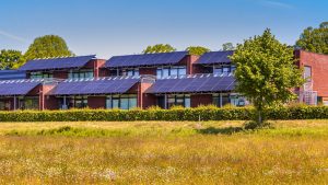 A modern brick building with large solar panels on the roof, showcasing expert Solar Panel Installation Lafourche Parish, surrounded by greenery and a grassy field under a clear blue sky.