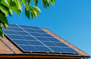 Solar Panel Installation Lafourche Parish: Solar panels are installed on the roof of a house under a clear blue sky, with green leaves partially visible in the foreground.